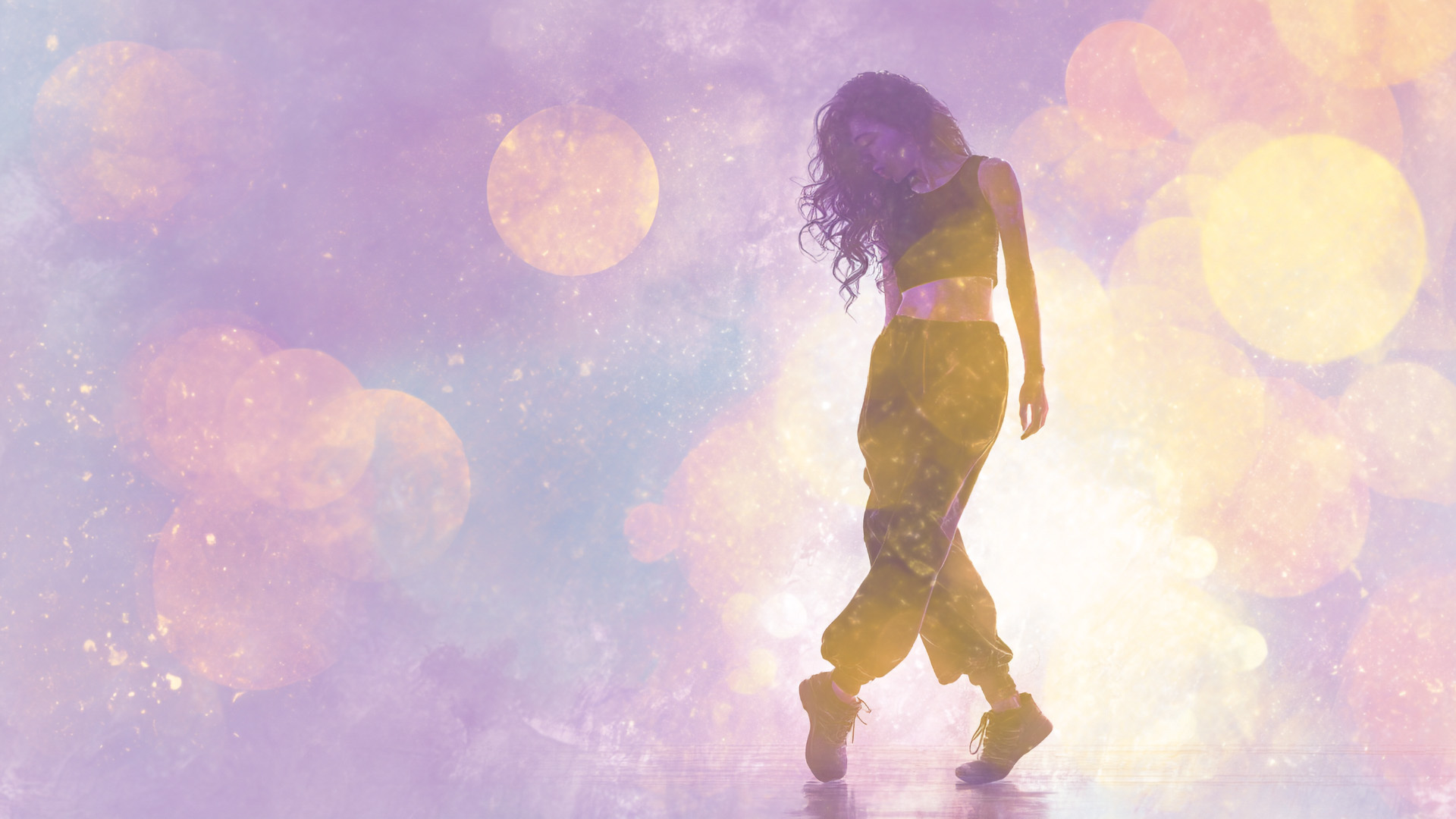 A woman with long, wavy hair dances with courage in loose pants and a crop top, silhouetted against a dreamy, pastel background filled with soft, glowing bokeh lights in shades of purple, pink, and yellow.