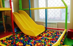 A colorful indoor play area with twisting tube slides emptying into a large ball pit filled with bright multicolored balls.
