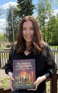 Lynn A. Haller, author of The Hallway of Doorknobs, smiling and holding her book outdoors on a sunny spring day.