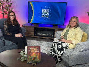 Lynn A. Haller, LCSW, author of The Hallway of Doorknobs, seated in the Fox 8 News Now studio with host KC O'Day. The book is displayed on the coffee table between them.